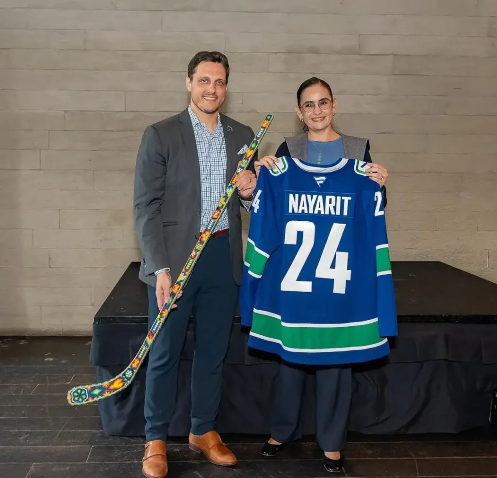 Dos personas sosteniendo un palo de hockey adornado con chaquira en patronas wixárikas y un jersey personalizado